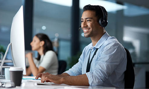 Shot of a young man using a headset and computer in a modern office