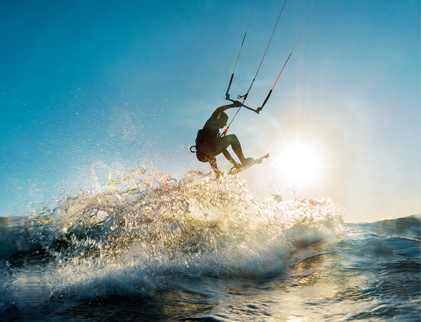 A surfer doing an amazing jump and splashing water in front of the sunset at the sea